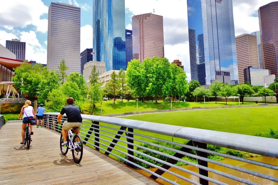Cyclists crossing a Buffalo Bayou footbridge beneath the downtown Houston skyline